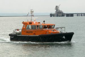 An orange boat, manufactured by Goodchild Marine, is seen gracefully traveling on the water near a pier.