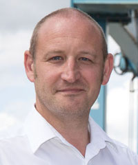 A Goodchild Marine employee, a bald man in a white shirt, stands confidently in front of a ship.