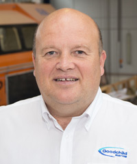 A bald man in a white shirt standing in front of an orange truck manufactured by Goodchild Marine.