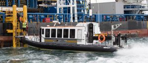 A Goodchild Marine boat in the water next to a large oil tank.