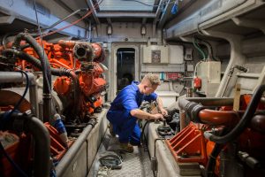 A man is working on an engine inside a Goodchild Marine boat.