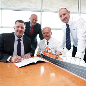 Four men signing a document at a table with a model of the boat built by Goodchild Marine.