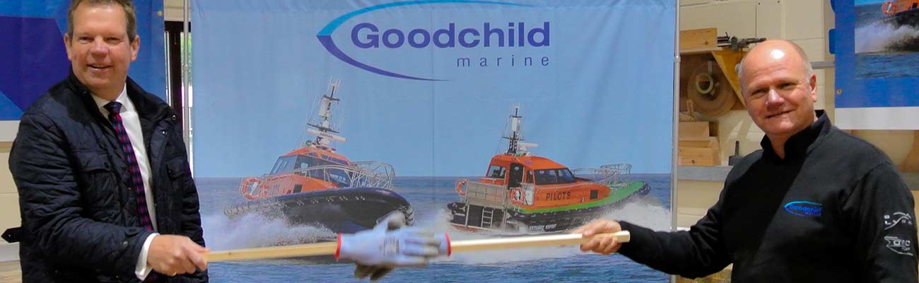 Two men holding a shovel in front of a Goodchild Marine boat.