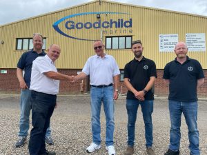A group of men shaking hands in front of a Goodchild Marine factory.
